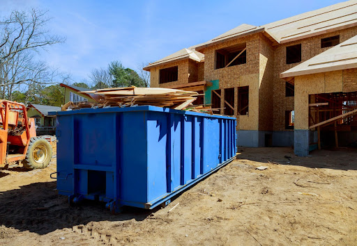 A blue dumpster sits filled at a residential construction project.