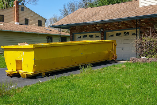 A yellow dumpster in a residential driveway.