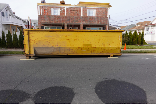 A yellow dumpster sits on a street outside of a brick home.